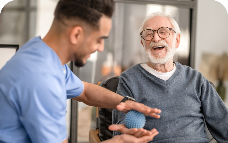 Caregiver teaching blue stress-ball exercise to elderly patient