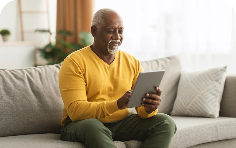Man in a yellow sweater using a tablet on a couch in a cozy living room