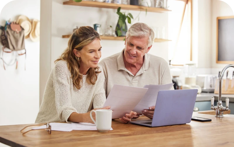 A man and woman review documents at a table with a laptop and coffee