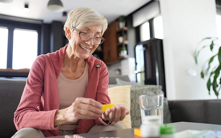 Elderly woman smiling while taking medication from a pill organizer