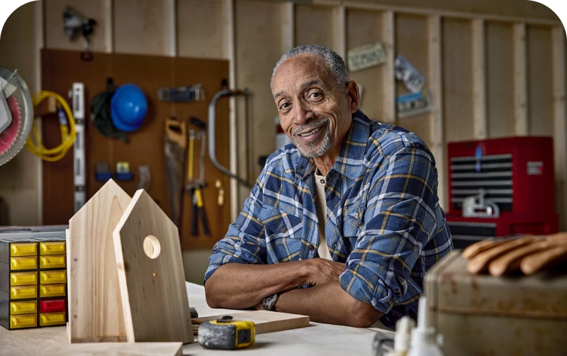 Person at a workbench with woodworking tools and a partially built birdhouse.