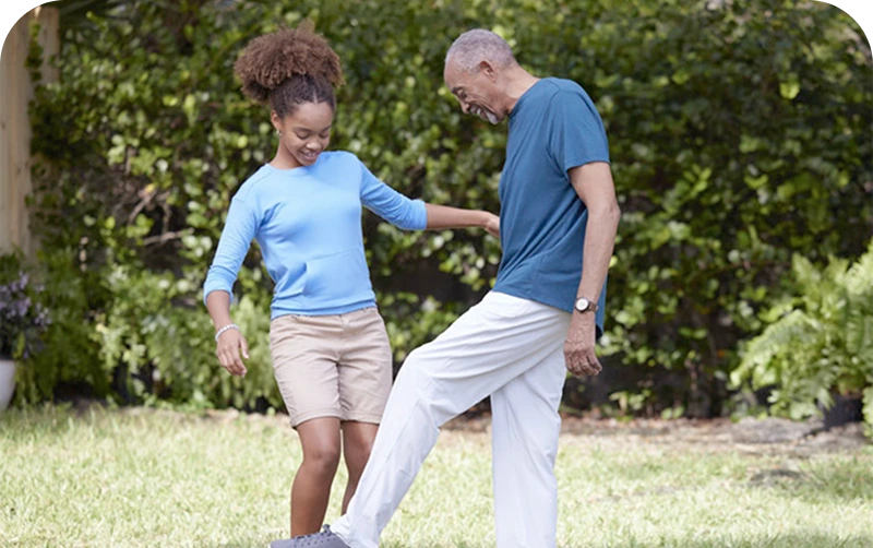 An adult and a child play soccer together on grass, smiling and enjoying their time in a sunny backyard
