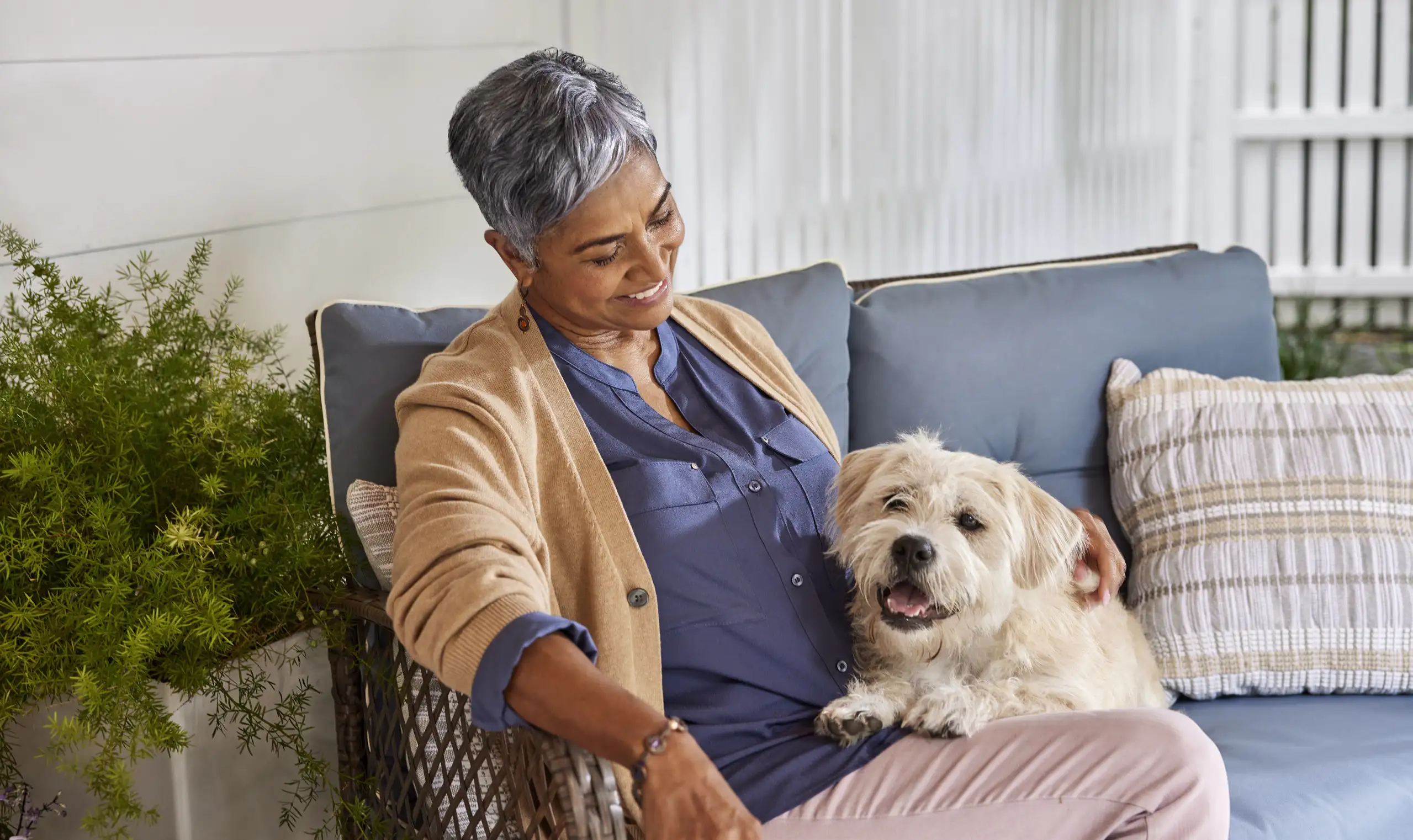 An elderly woman relaxes on a couch with a fluffy dog beside her