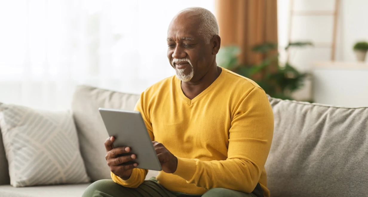 Man in a yellow sweater using a tablet on a couch in a cozy living room