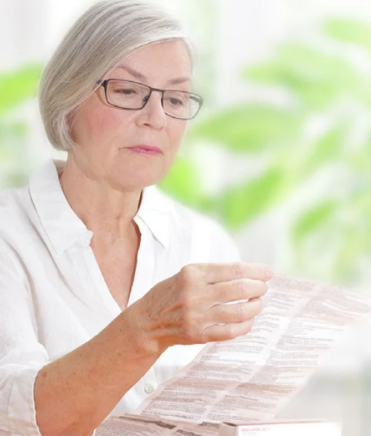 Elderly person in a white shirt holding a document in a bright room with plants
