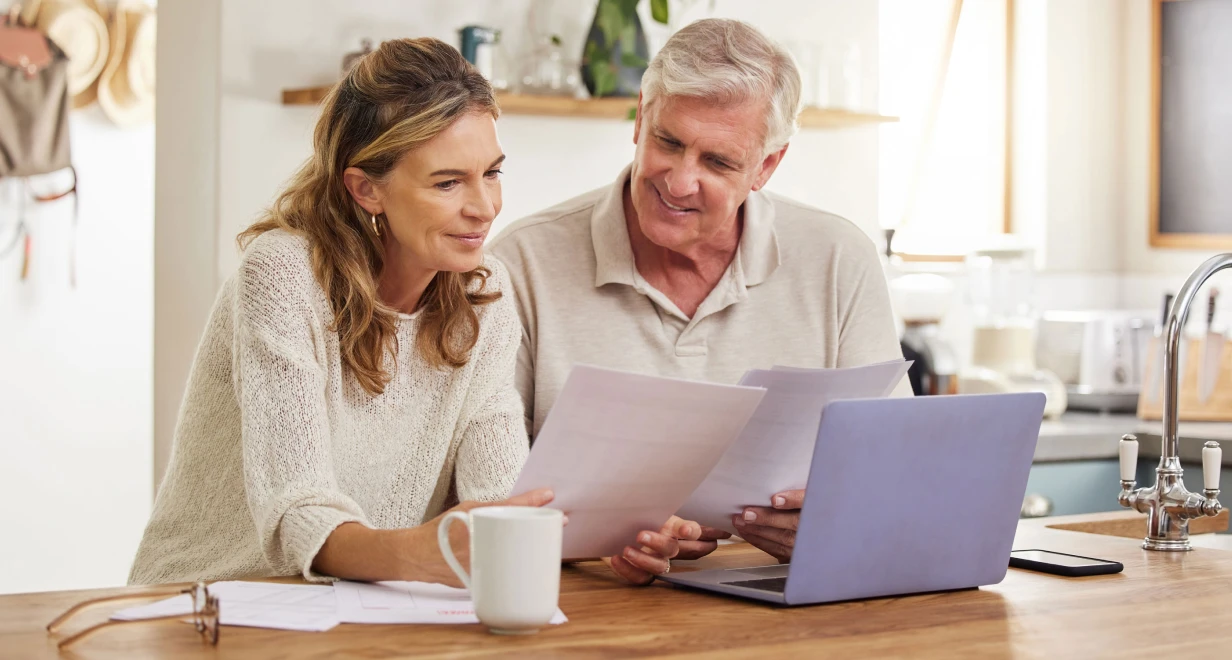 A man and woman review documents at a table with a laptop and coffee