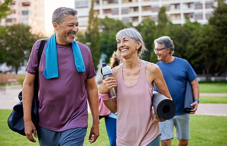 Smiling older man and woman walking outdoors with exercise gear, enjoying a conversation