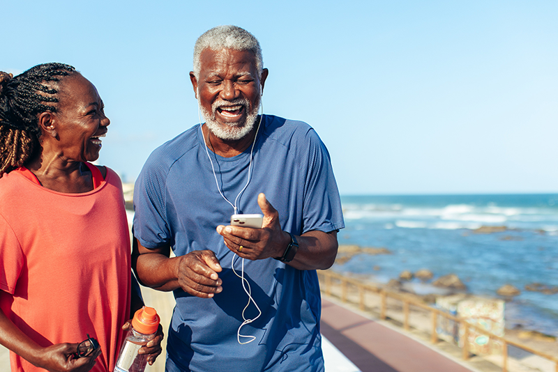 Happy older couple jogging outdoors, smiling and enjoying each other's company while holding water bottles and a phone.