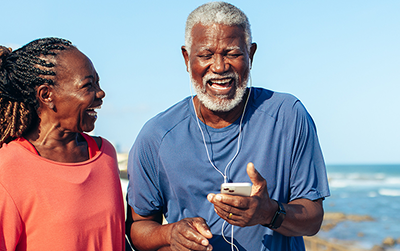 Happy older couple jogging outdoors, smiling and enjoying each other's company while holding water bottles and a phone.