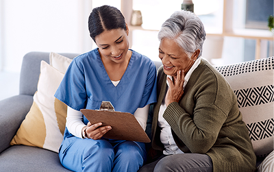 Nurse reviews medical chart with smiling elderly woman on couch
