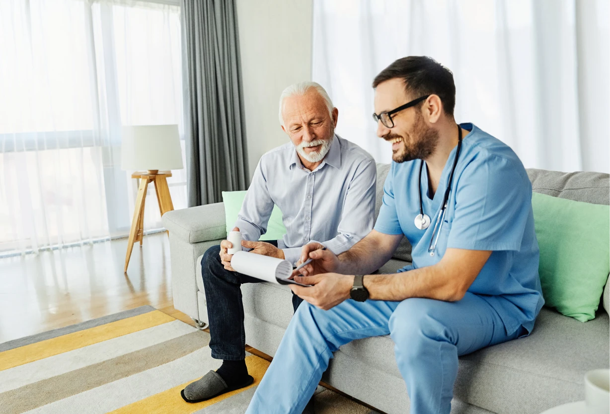 Healthcare worker in scrubs reviewing documents with an elderly man in a living room setting