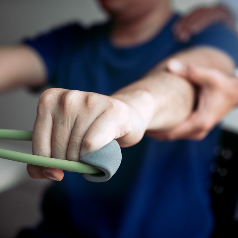 Physical therapist supporting patient's forearm during resistance band exercise.