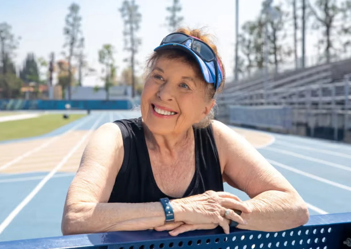 Senior woman runner smiles at track, wearing fitness tracker