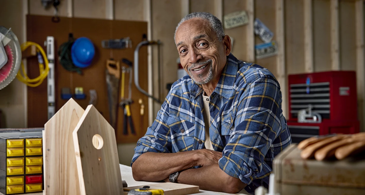 Person at a workbench with woodworking tools and a partially built birdhouse