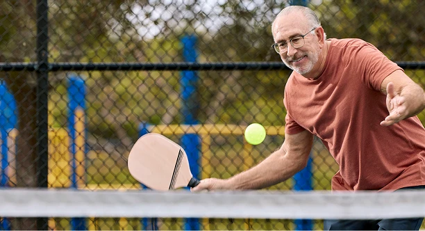 An older man swings a tennis racquet while playing on an outdoor court