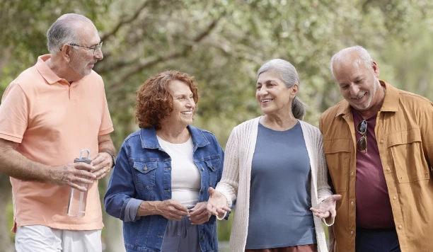 A group of four adults stands together outdoors, engaged in conversation amidst blurred greenery in the background