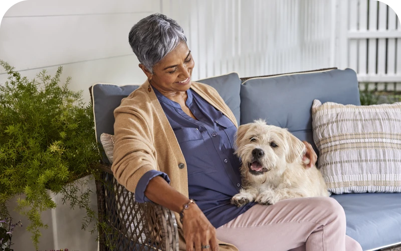 An elderly woman relaxes on a cozy couch, gently petting a fluffy dog