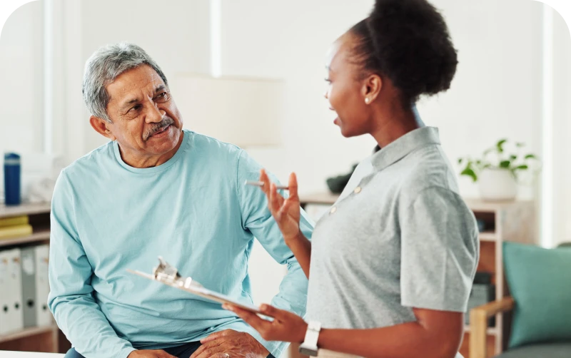 A woman discussing something with a man in a light blue sweater, holding a clipboard in a bright room